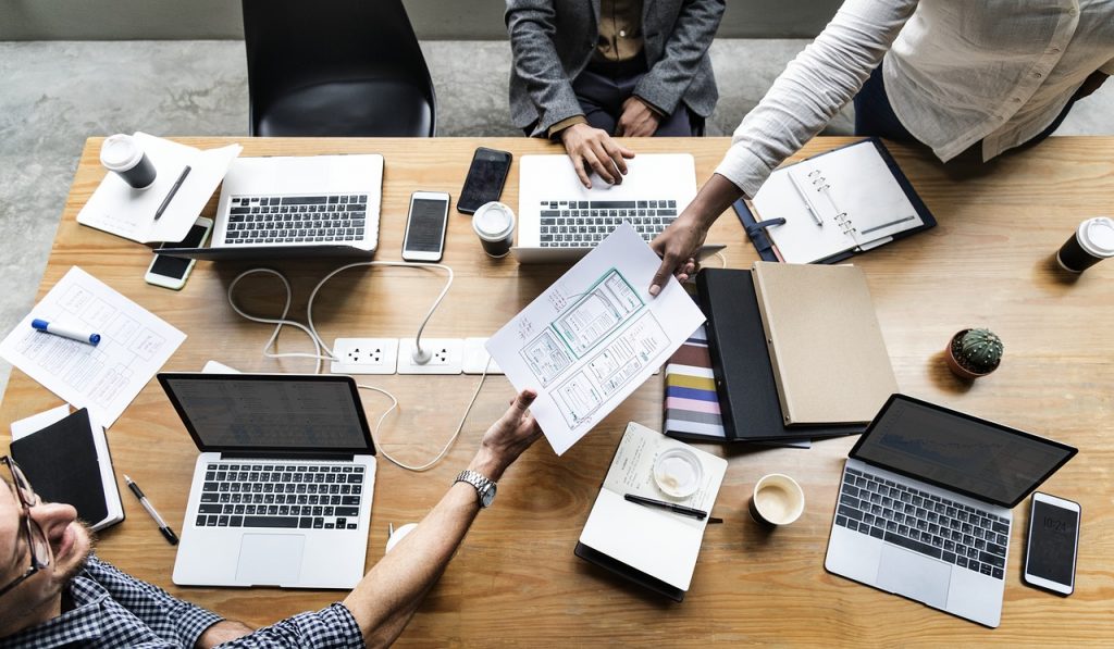 a person sitting at a table with several laptops and papers on it