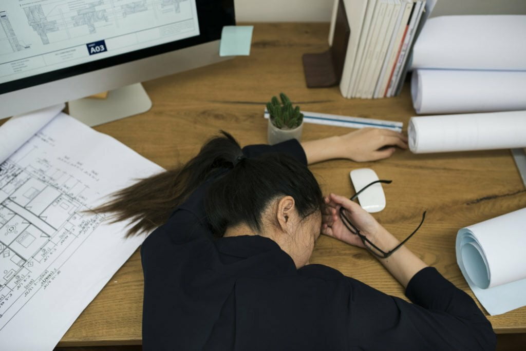 a person with long hair sitting at a desk with a computer and a plant in the hand