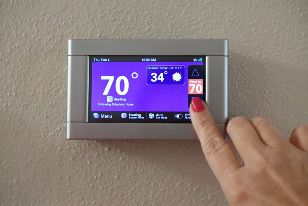 Female adjusting modern digital thermostat control pad in home to set heating cooling temperatures