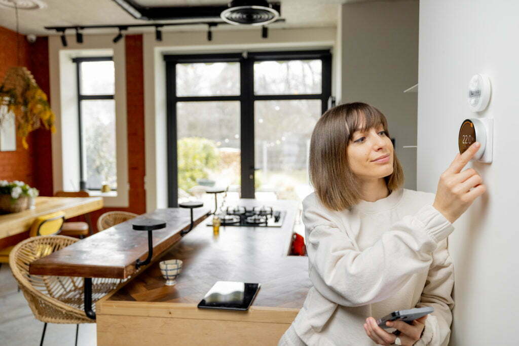 Woman controlling home temperature with electronic thermostat