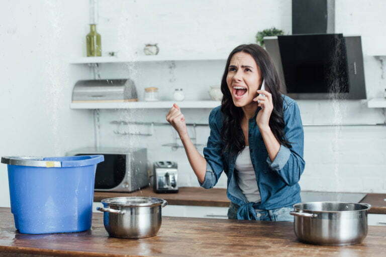 Angry woman calling plumber during leak in kitchen