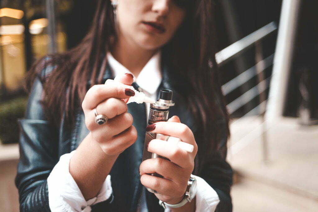 Woman refills liquid in e-cigarette closeup. Girl refills liquid in vape.