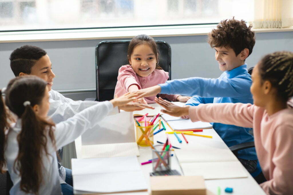 Diverse small school kids putting hands together at classroom