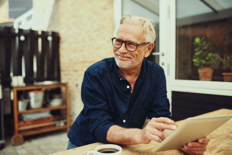 Senior man smiling while drinking coffee and using a tablet