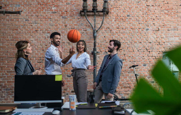 Group of cheerful young businesspeople playing basketball in office, taking a break