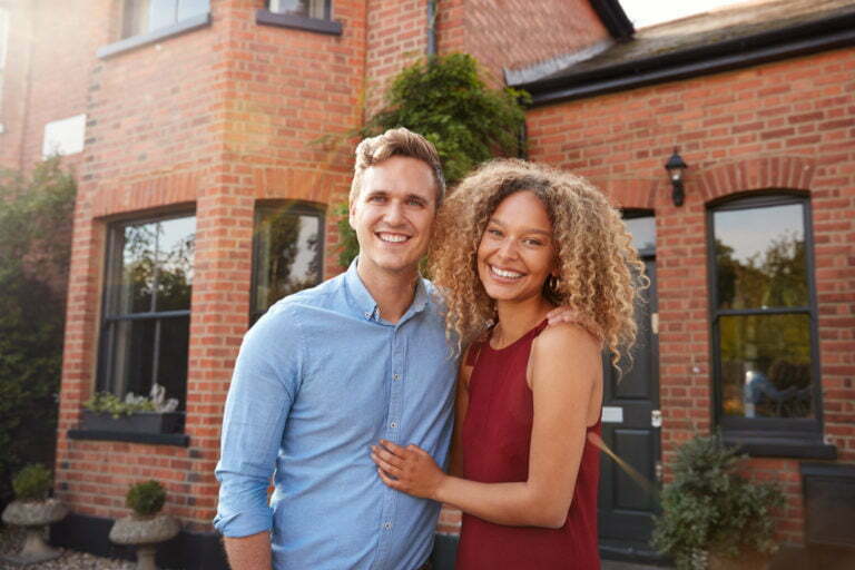 Portrait Of Excited Young Couple Standing Outside New Home Together